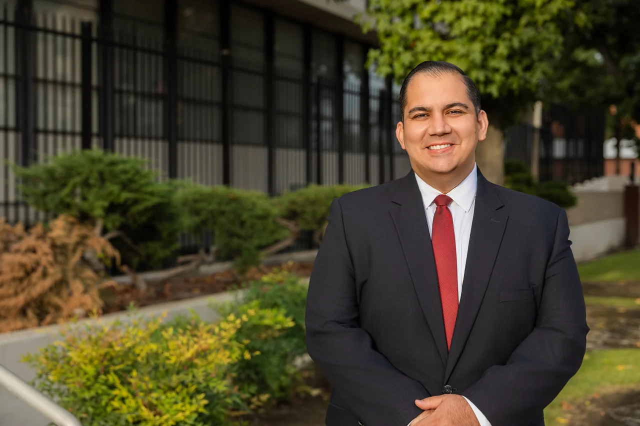 Pedro Naveiras smiling outdoors in a navy suit and red tie